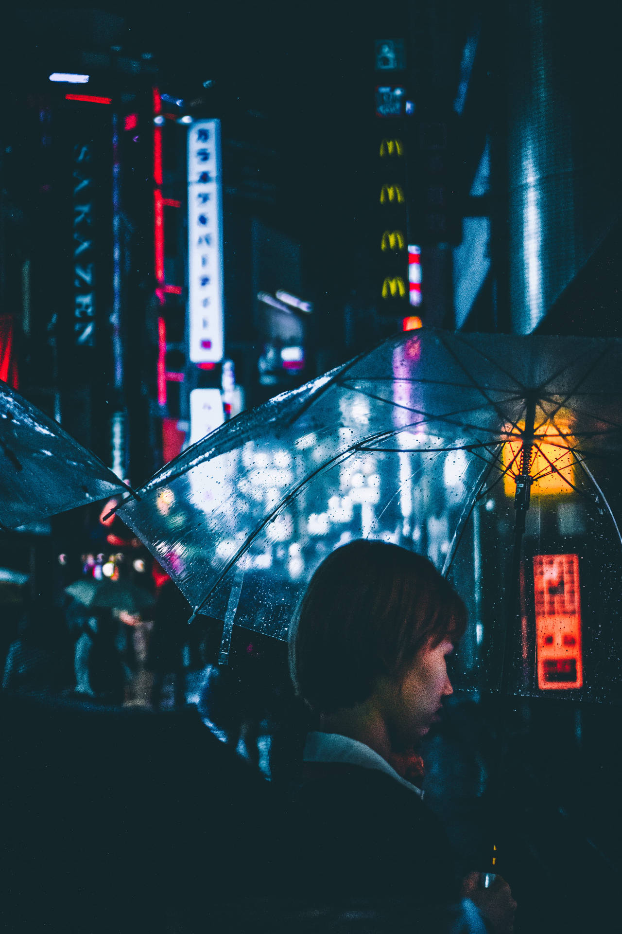夜晚喺落雨嘅霓虹城市入面揸住透明遮嘅人。