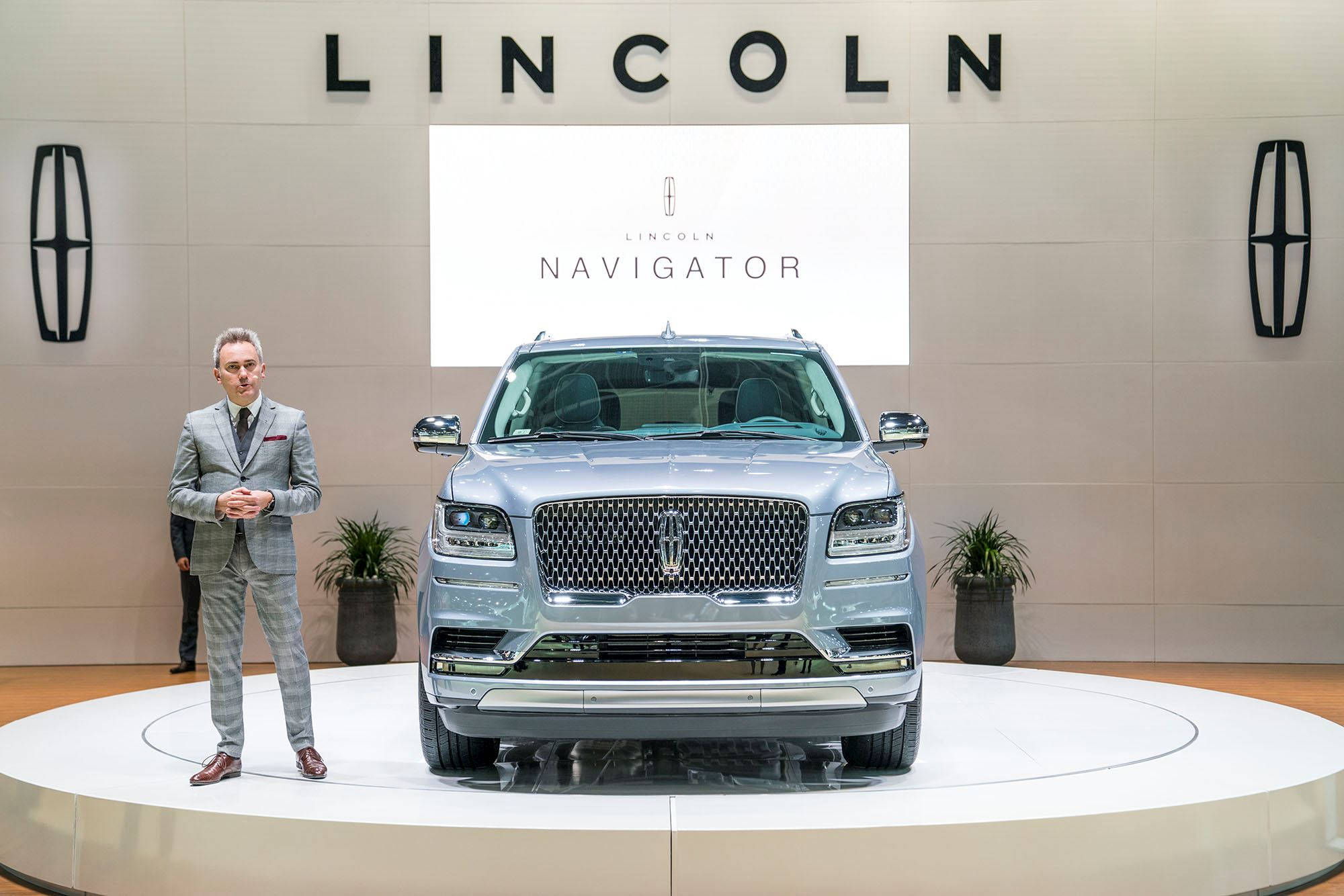 藍鑽金屬塗裝林肯Navigator豪華SUV 壁紙 — 一輛銀色林肯領航員SUV在車展的圓形平台上展示，旁邊站著一位講解員，在明亮的燈光下。