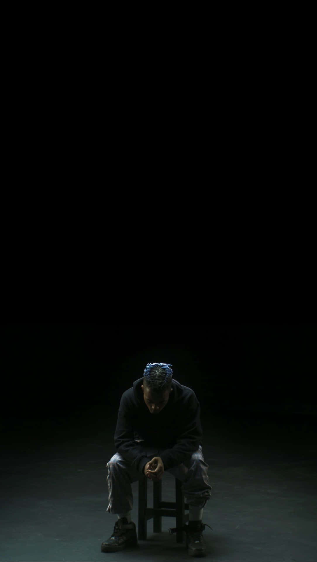 一個人在聚光燈下的黑暗中獨自坐在凳子上。