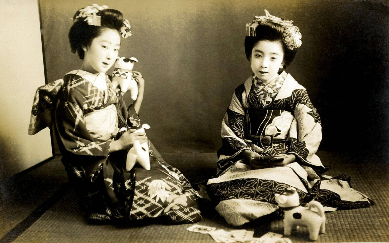 兩位年輕藝妓穿著傳統和服在榻榻米上手持人偶。