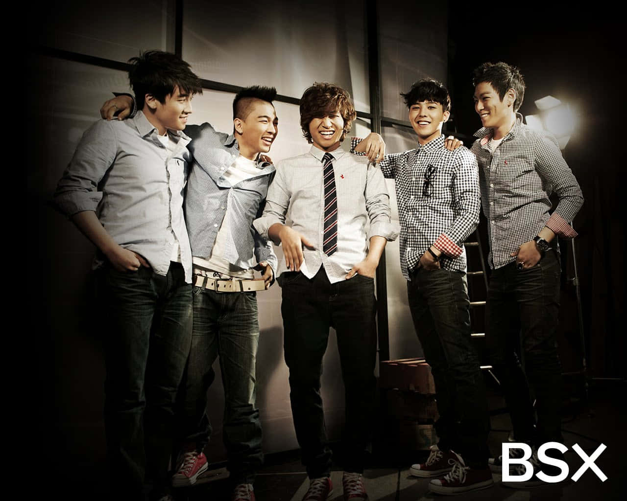 藝術啟發的BIGBANG成員影像 壁紙 — 五位微笑的年輕男士穿著休閒襯衫和牛仔褲，在深色攝影棚背景下互相搭肩合照。