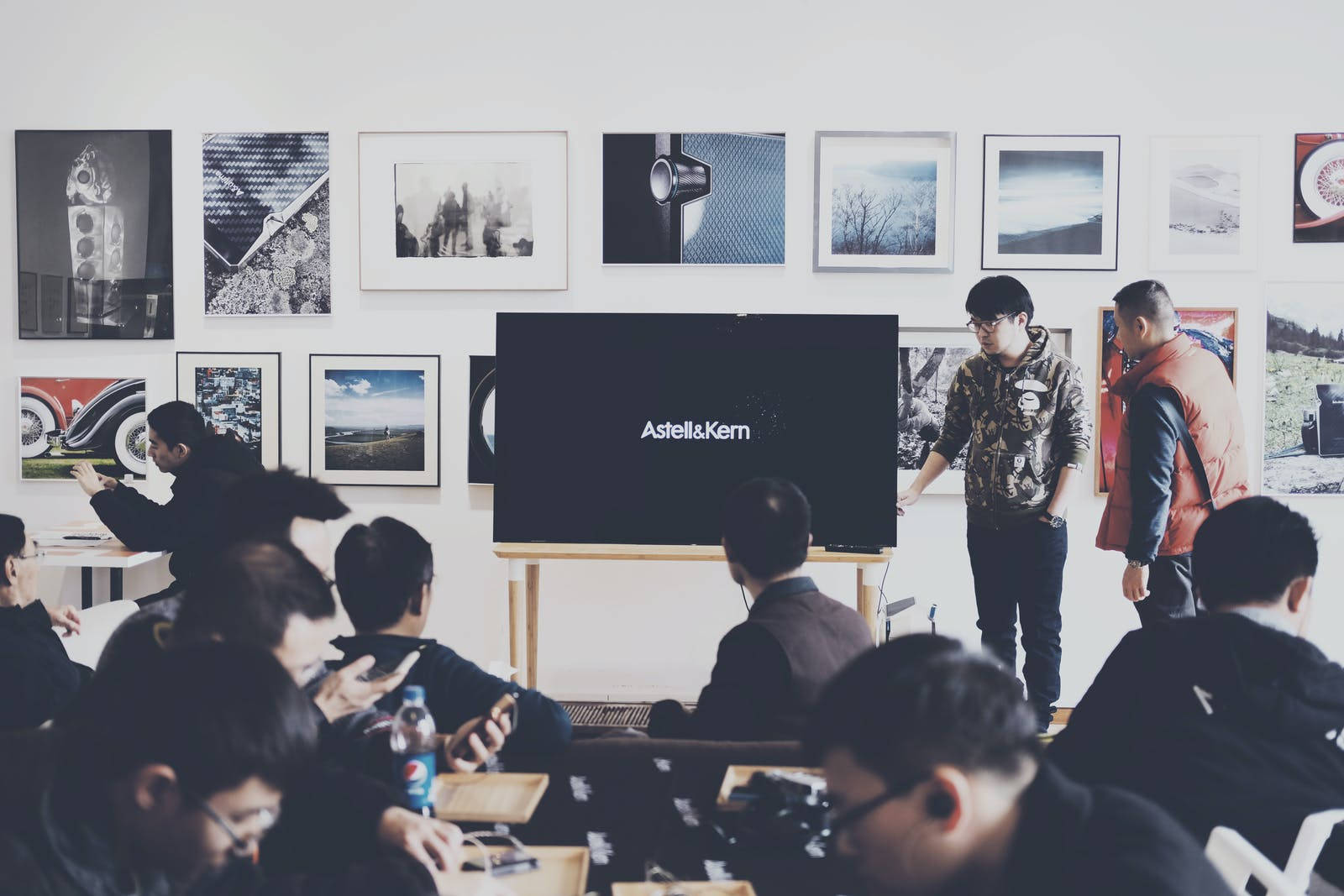 一位演講者在一個有裱框藝術品和顯示AstellKern的屏幕的房間裡向觀眾講話。