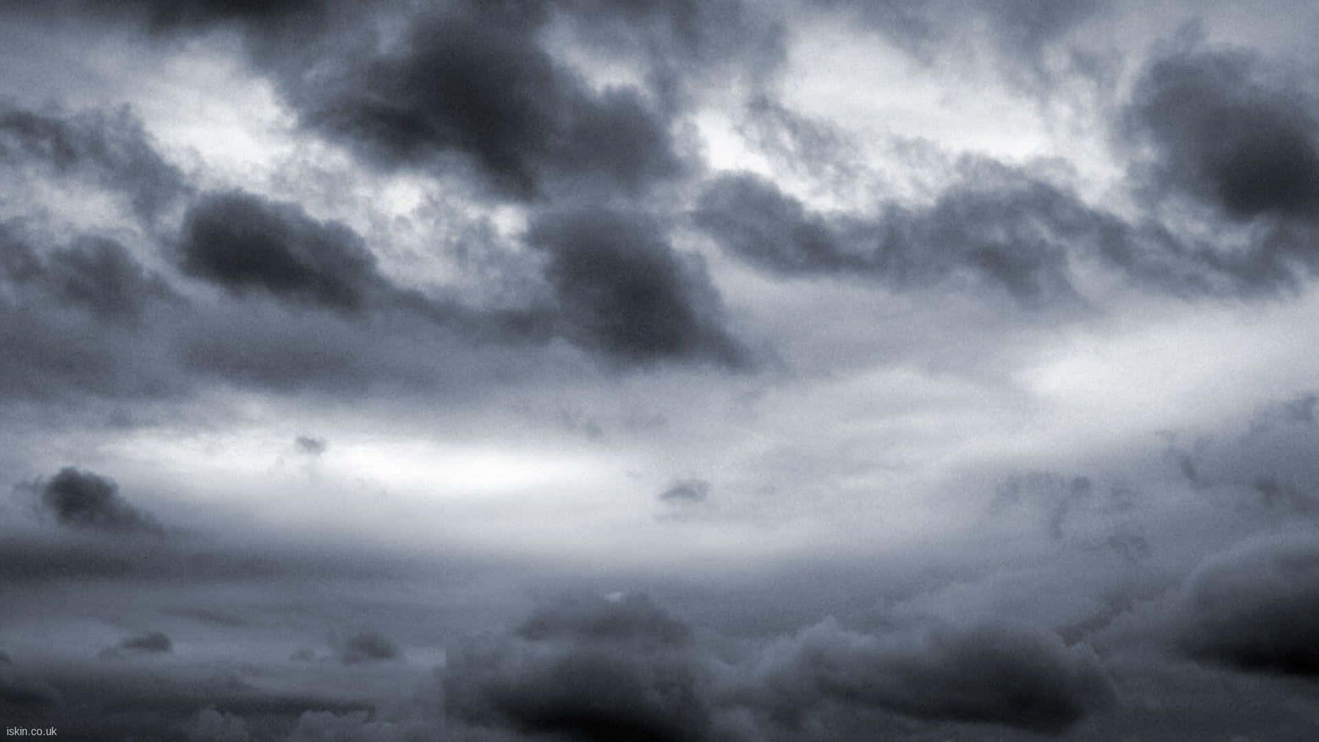 藝術感的暴風雨夜空 壁紙 — 戲劇性的風暴雲在陰鬱的黑白天空中旋轉，有明亮的陽光斑塊穿透而出。