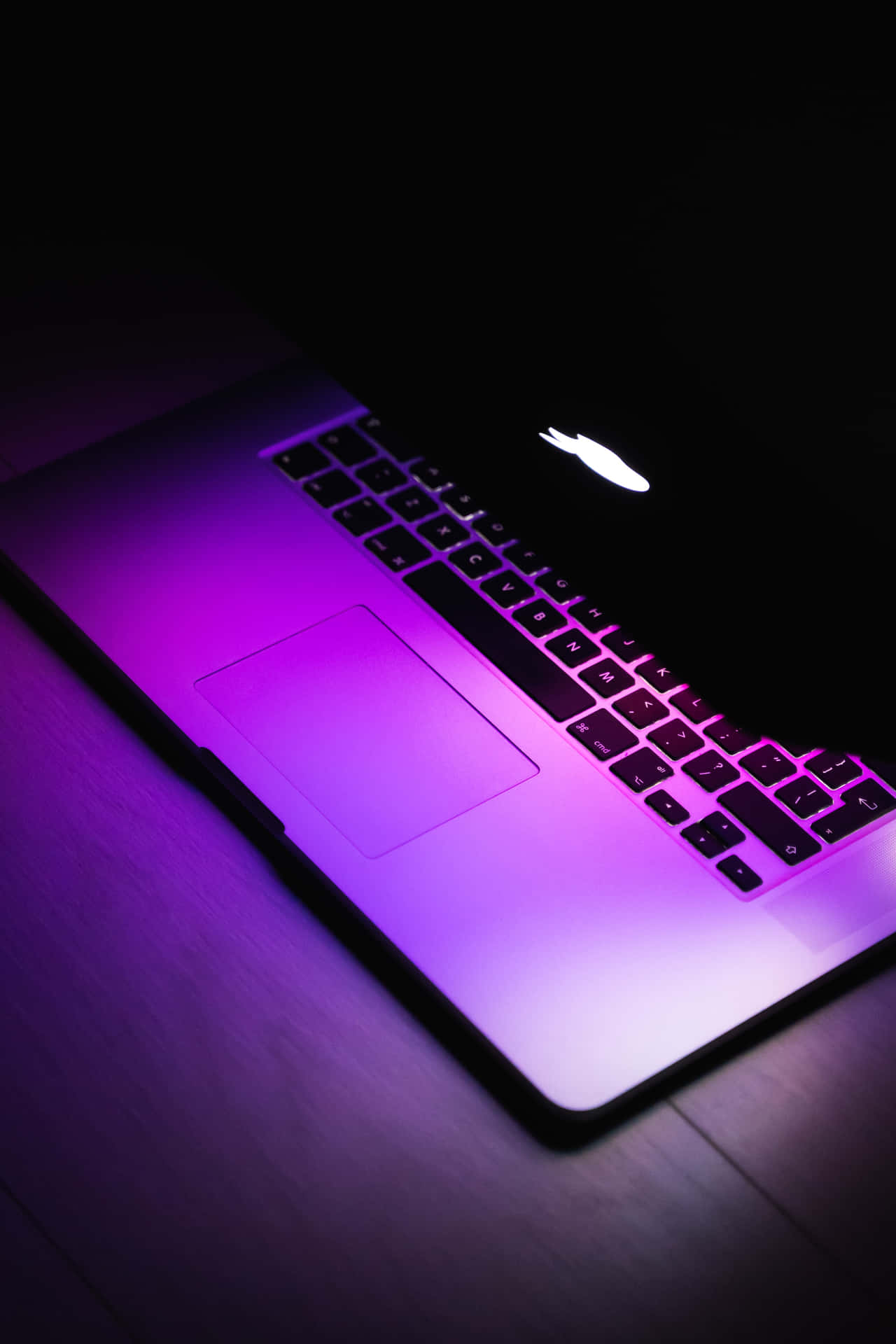 在黑暗中，木桌上發光的紫色筆記型電腦。