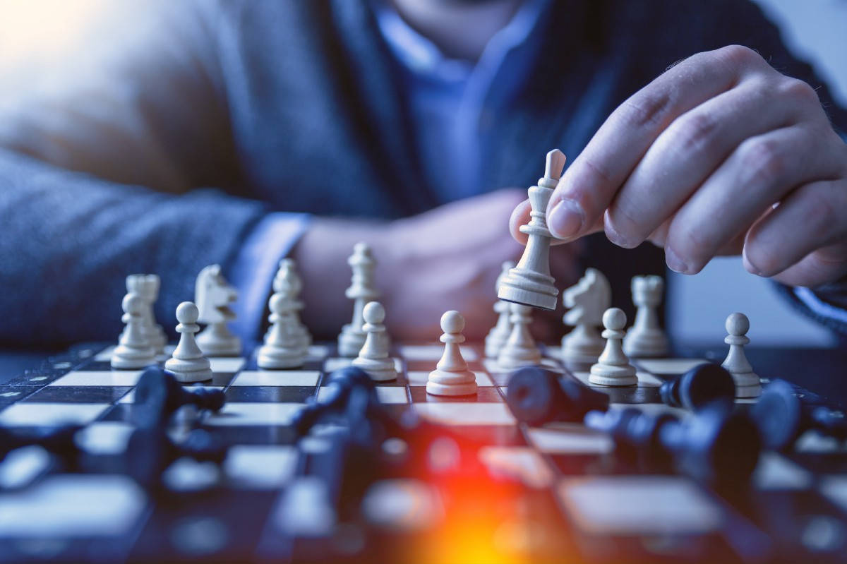 藝術感象棋攝影 壁紙 — 一隻手將白色國王棋提起，下方棋盤上有倒下的黑色棋子及發光的紅光特寫。
