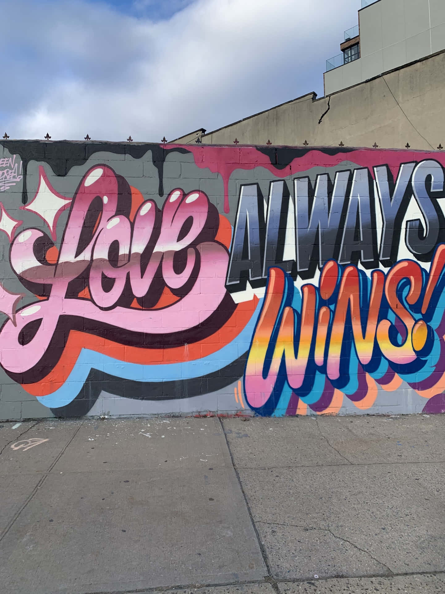 塗鴉壁畫，在陰天天空下的城市牆上寫著「Love Always Wins!」。