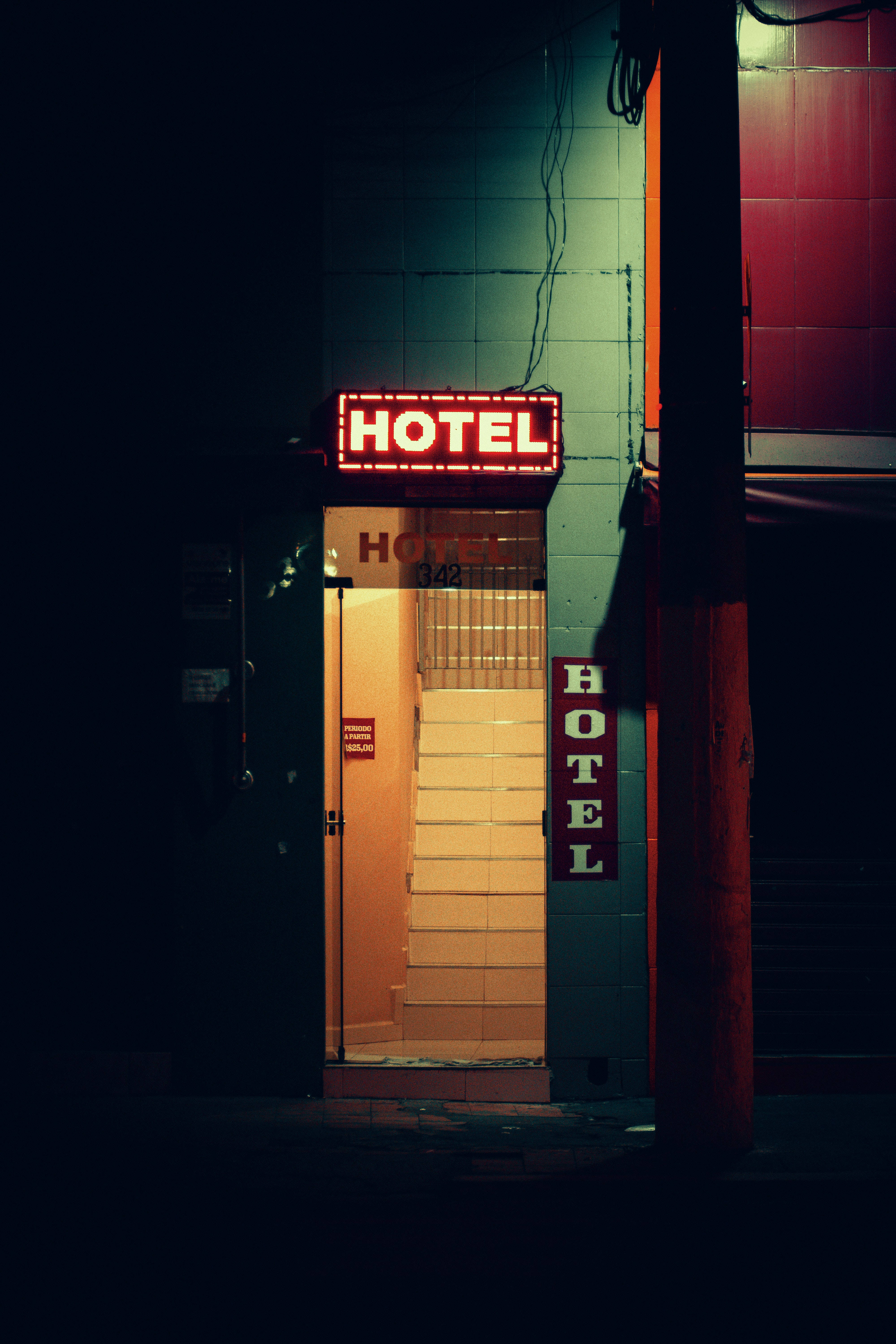 藝術風酒店入口 壁紙 — 一個發光的紅色霓虹燈酒店招牌在夜晚照亮了一條狹窄的小巷，將溫暖的光線投射在瓷磚樓梯和黑暗的牆壁上。