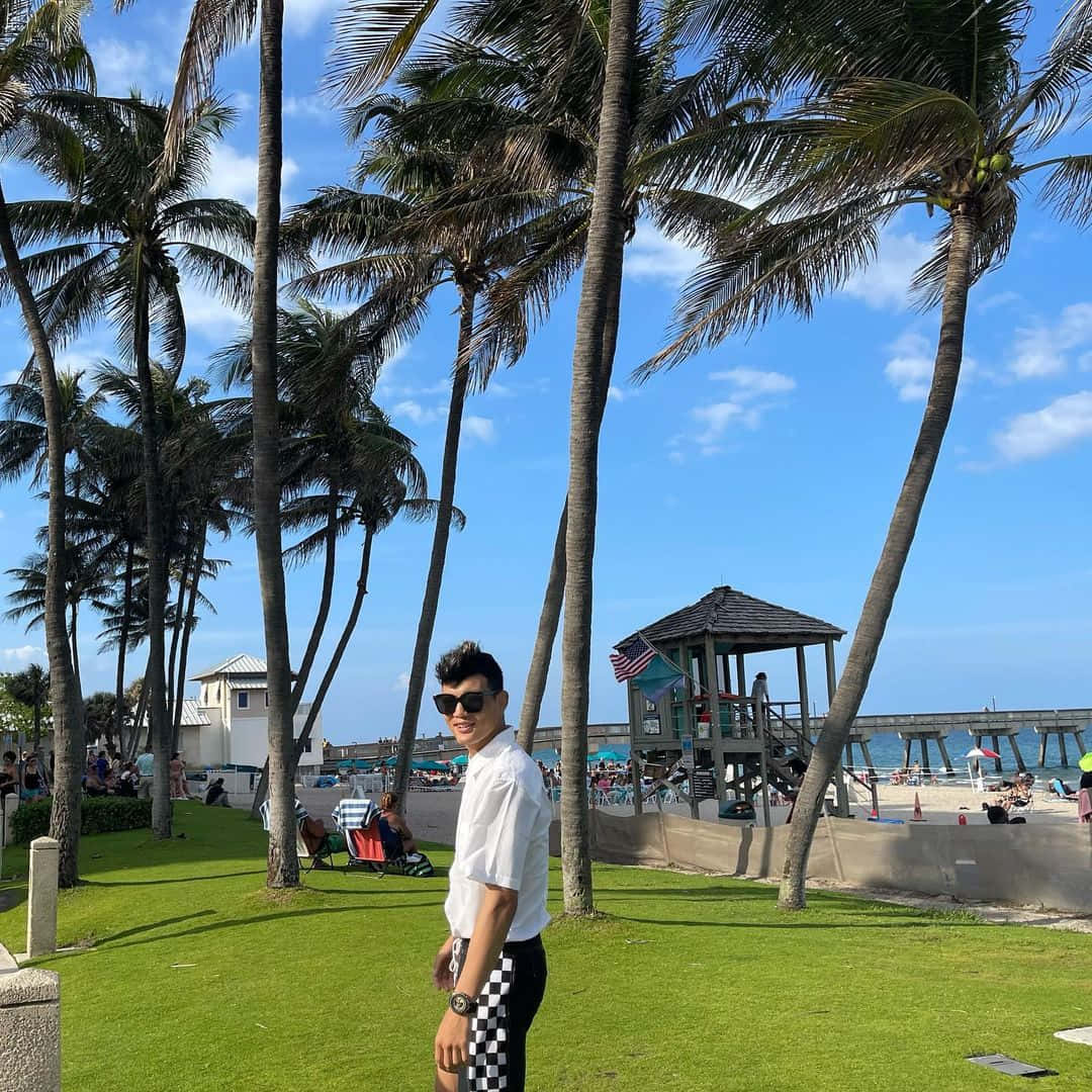 戴太陽眼鏡的男子在棕櫚樹和碼頭附近的海灘草地上擺姿勢