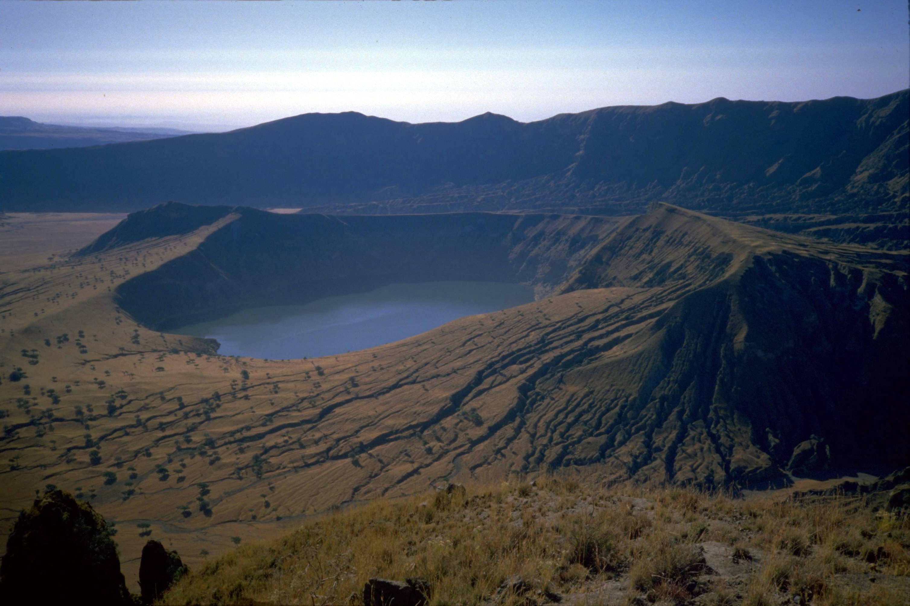 蘇丹傑貝爾馬拉 壁紙 — 一個廣闊的火山口湖，坐落在崎嶇的大地色山丘中，在清澈的藍天下。