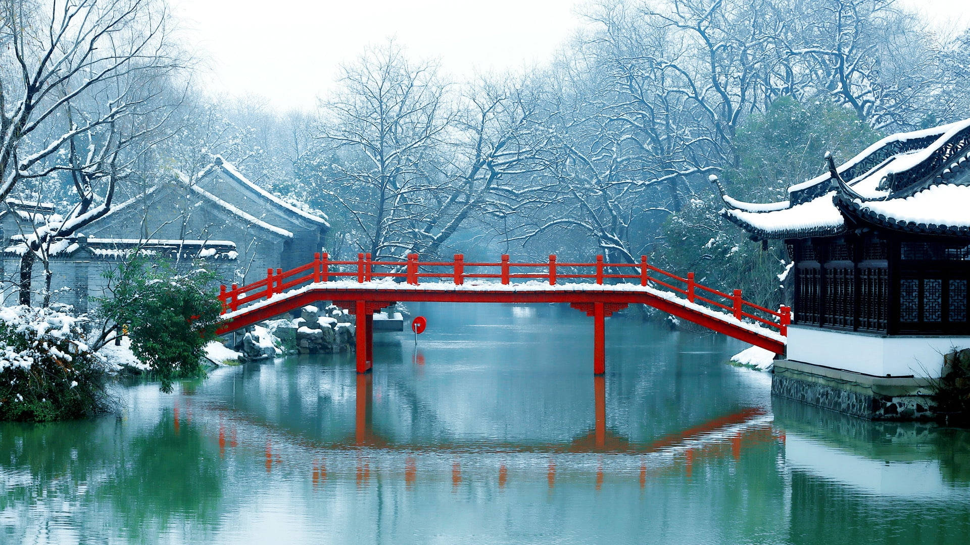 蘇州古典園林夕照美景 壁紙 — 一座鮮紅色的拱橋橫跨平靜的雪運河，在霧濛濛的冬日天空下映照出傳統東亞建築。