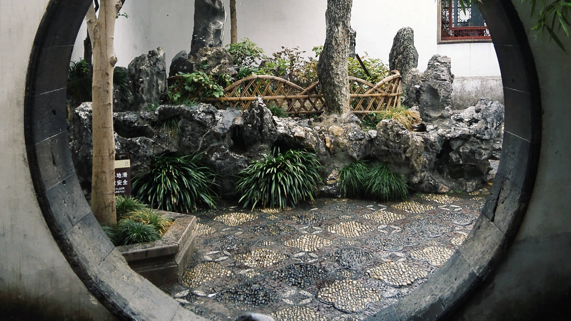 蘇州滄浪亭 壁紙 — 圓形石窗框住一個傳統中式花園，內有嶙峋岩石、竹子和馬賽克石徑。