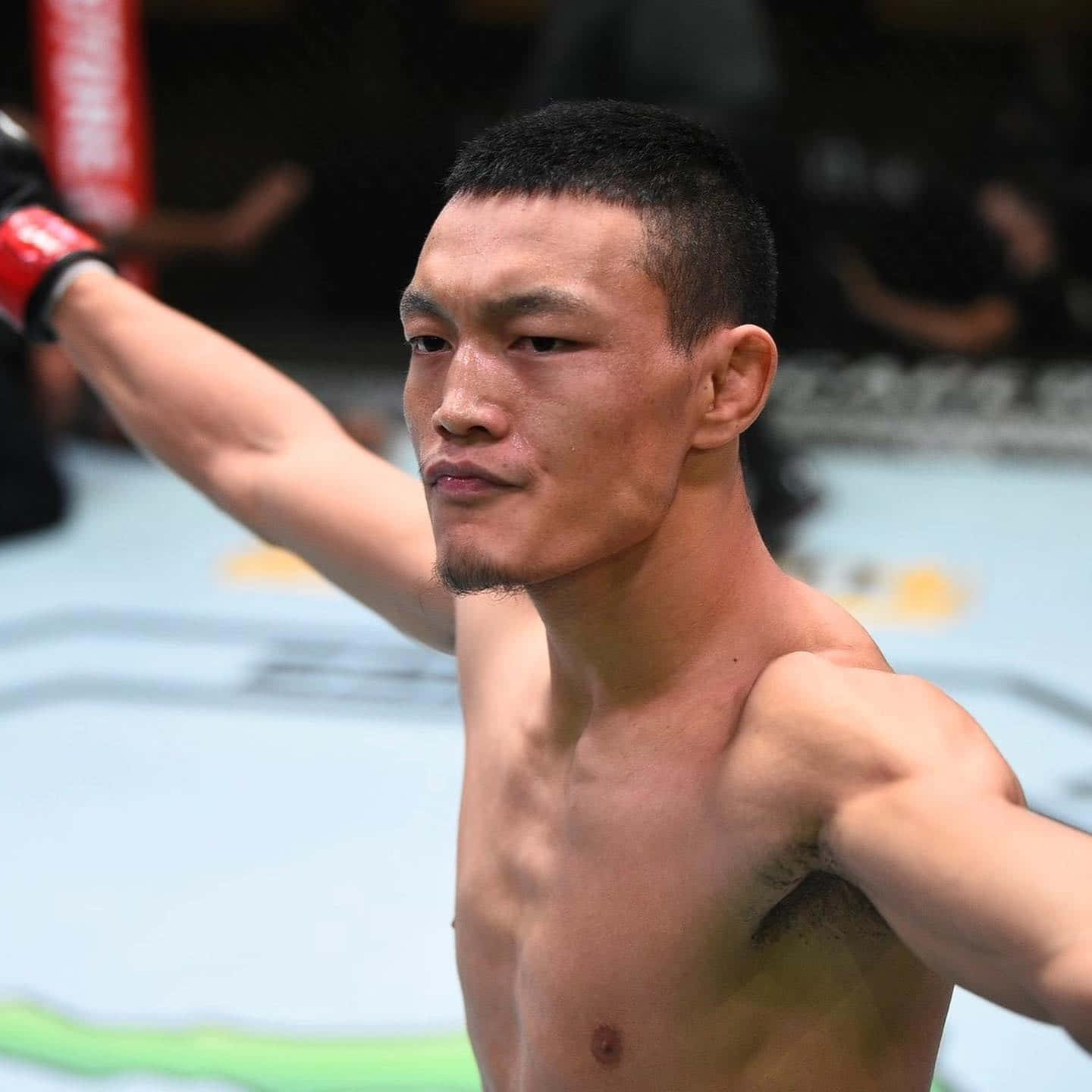 一位赤裸上身的MMA拳手在八角籠內舉起戴著紅色手套的拳頭慶祝勝利。