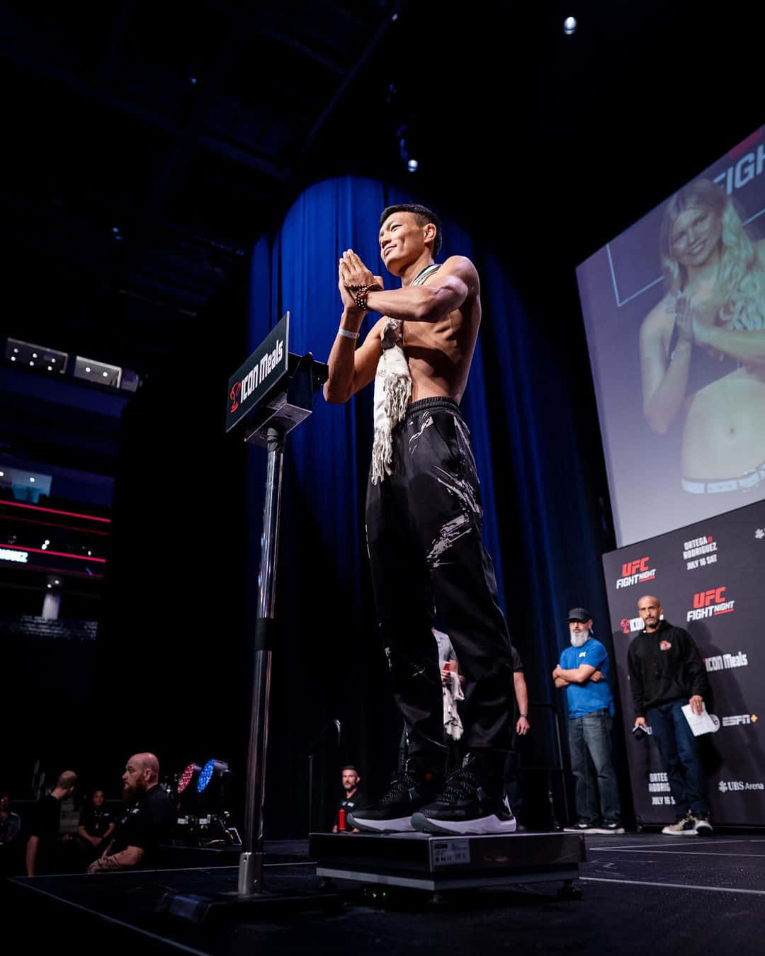 UFC戰士在稱重活動中站在體重秤上，身後有群眾和屏幕。