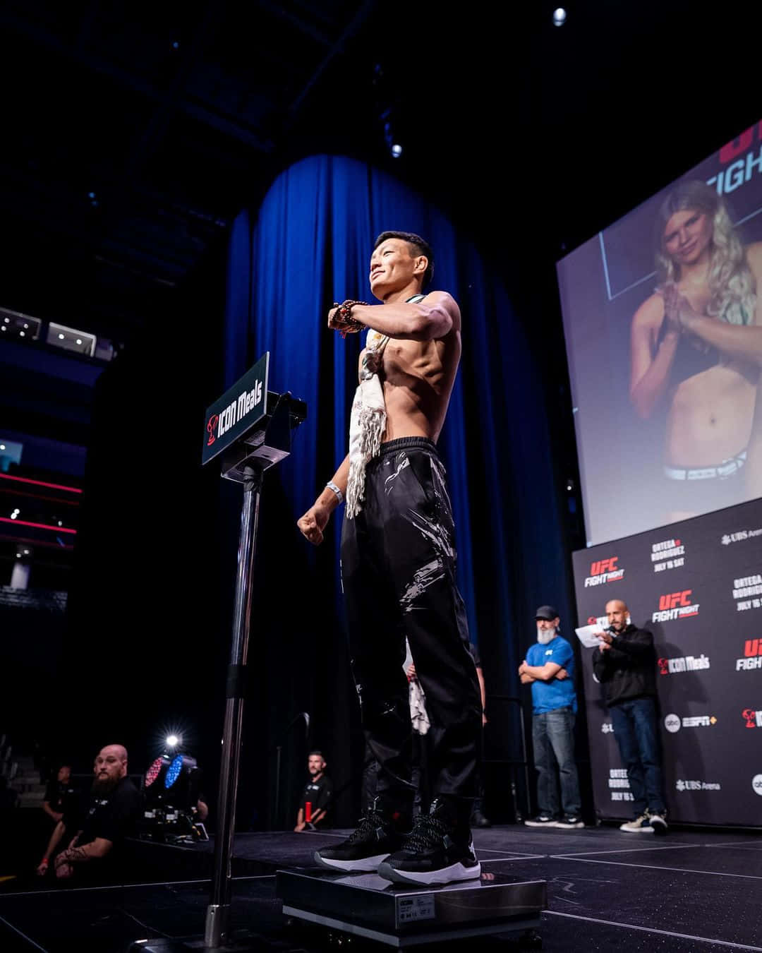 UFC拳手在稱重活動中站在體重磅上，屏幕顯示對手