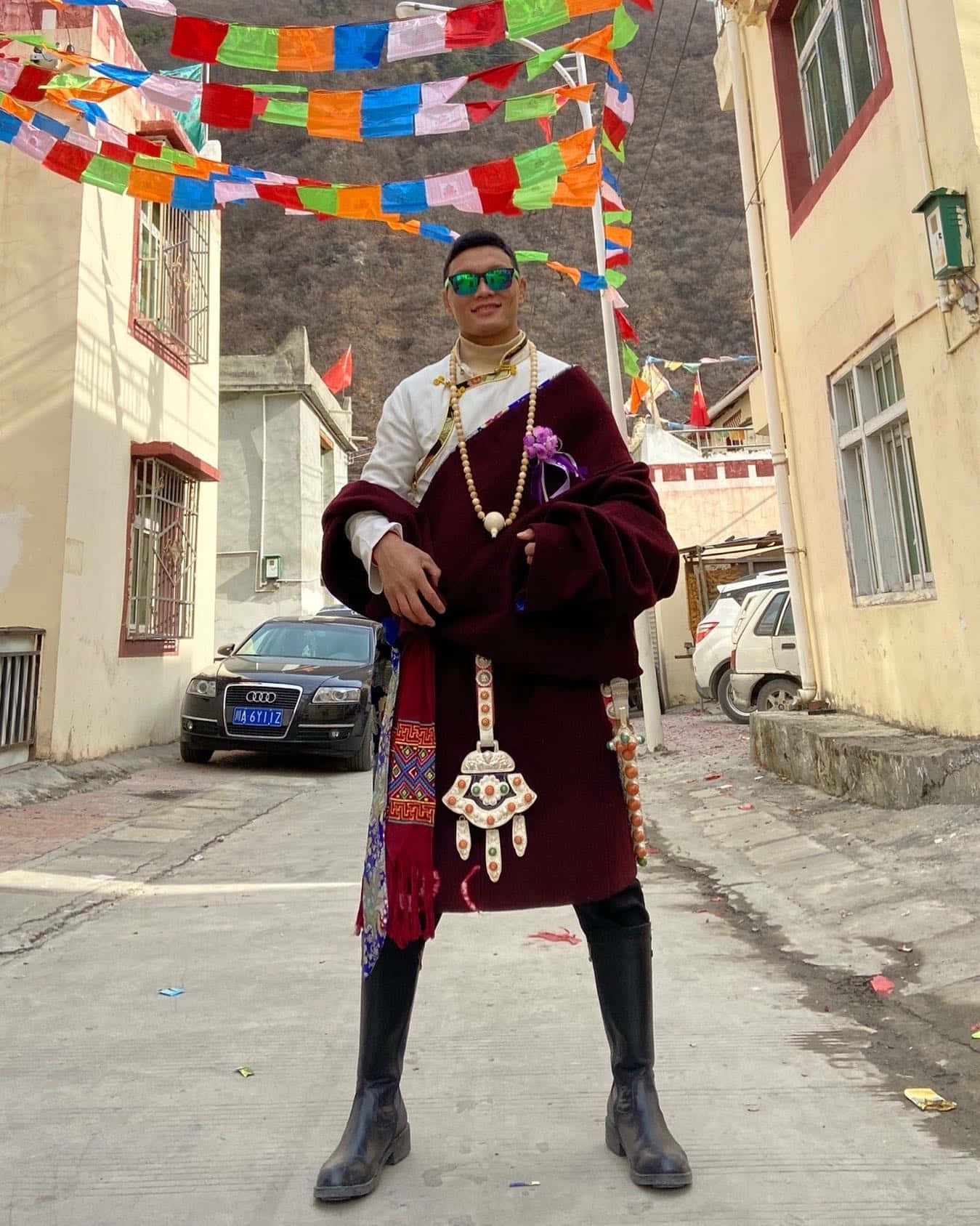 身穿傳統藏服的男子站在掛有經幡的街道上。