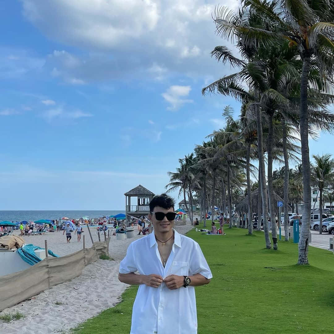 身穿白襯衫和太陽眼鏡的男子在擠滿棕櫚樹的海灘上微笑。