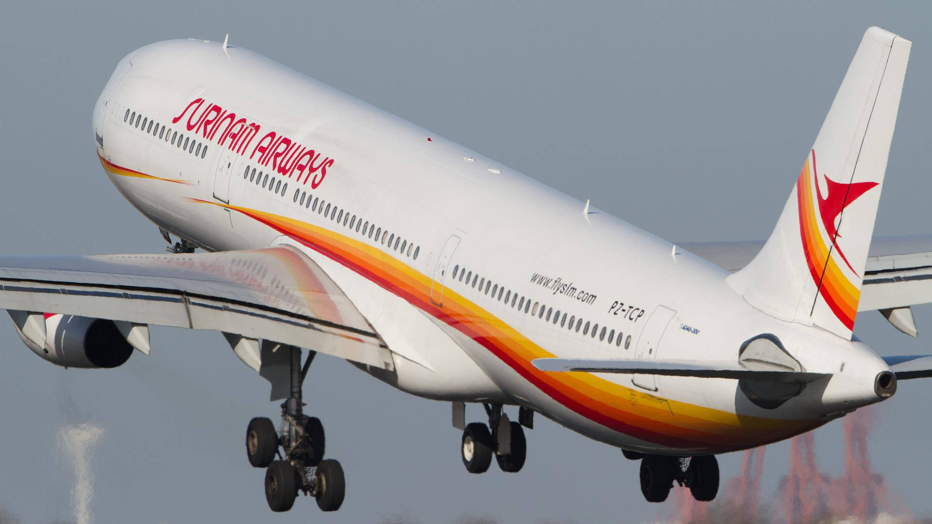 蘇里南飛機 壁紙 — 蘇利南航空一架紅橙黃色塗裝的空中巴士A340在起飛時急轉，背景是朦朧的天空。