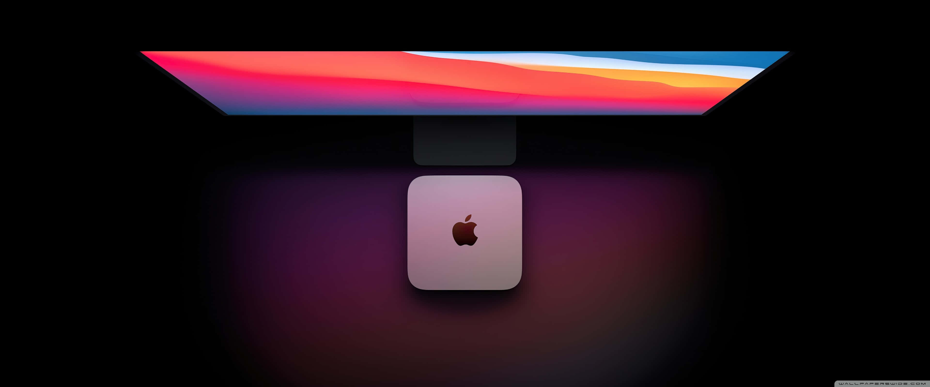 蘋果 3840x1600 解析度壁紙 壁紙 — 一部時尚的 Apple iMac 配備鮮豔的漸變顯示屏，放置在相配的 Mac Studio 之上，處於昏暗環境中。