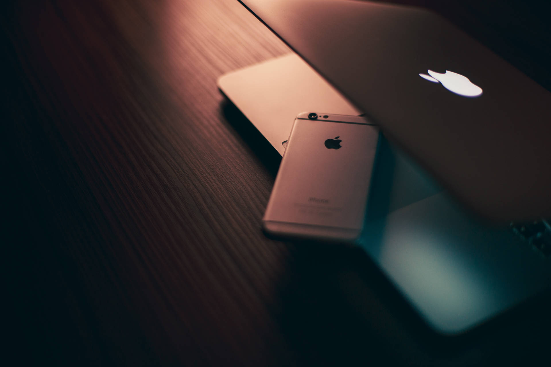 溫暖燈光下的深色木桌上，金色iPhone和MacBook。