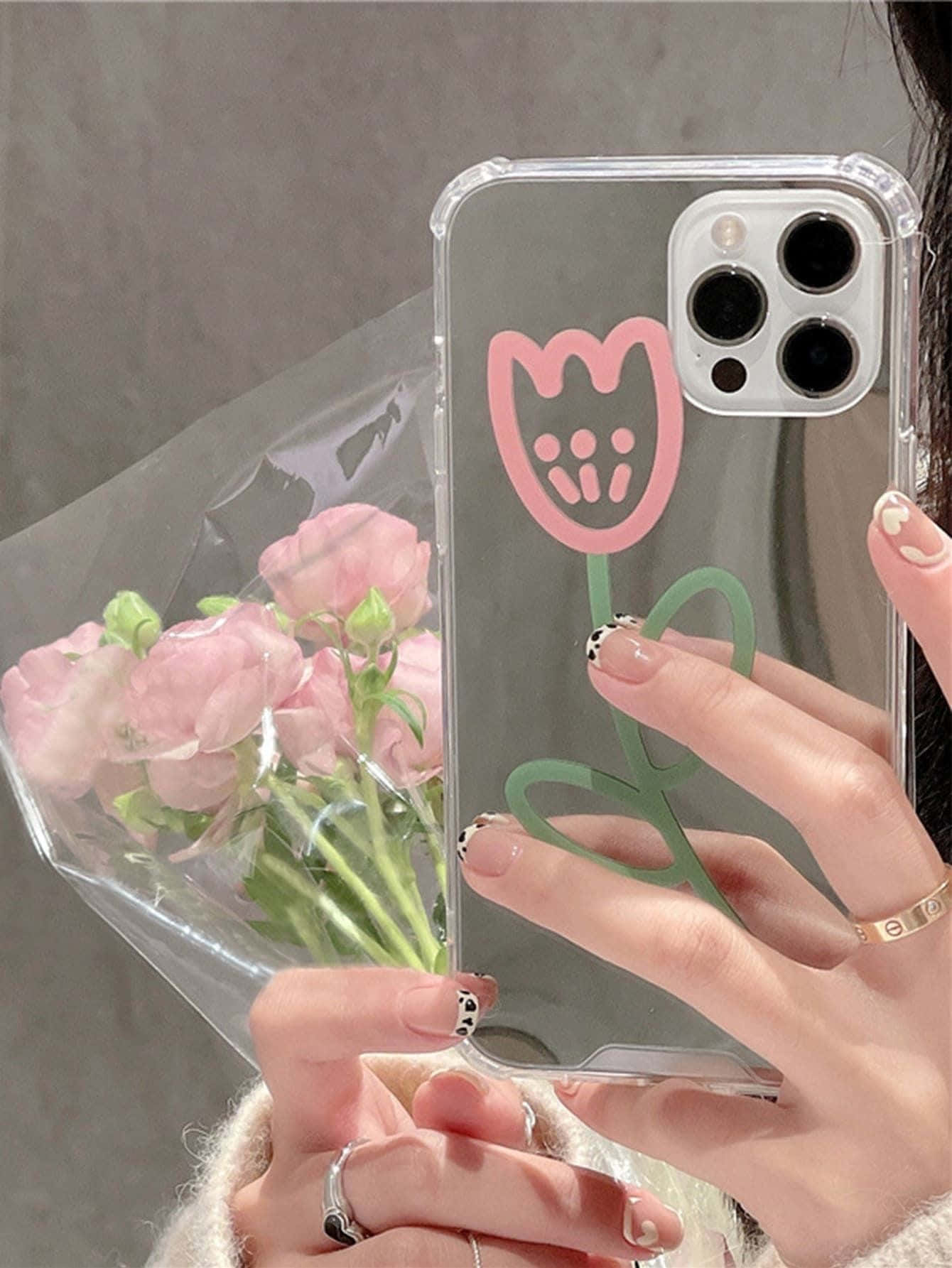 蘋果下一代 iPhone 12 —— 現已上市 壁紙 — 一隻手拿著一個帶有粉紅色鬱金香設計的透明手機殼，同時握著一束粉紅色的花。