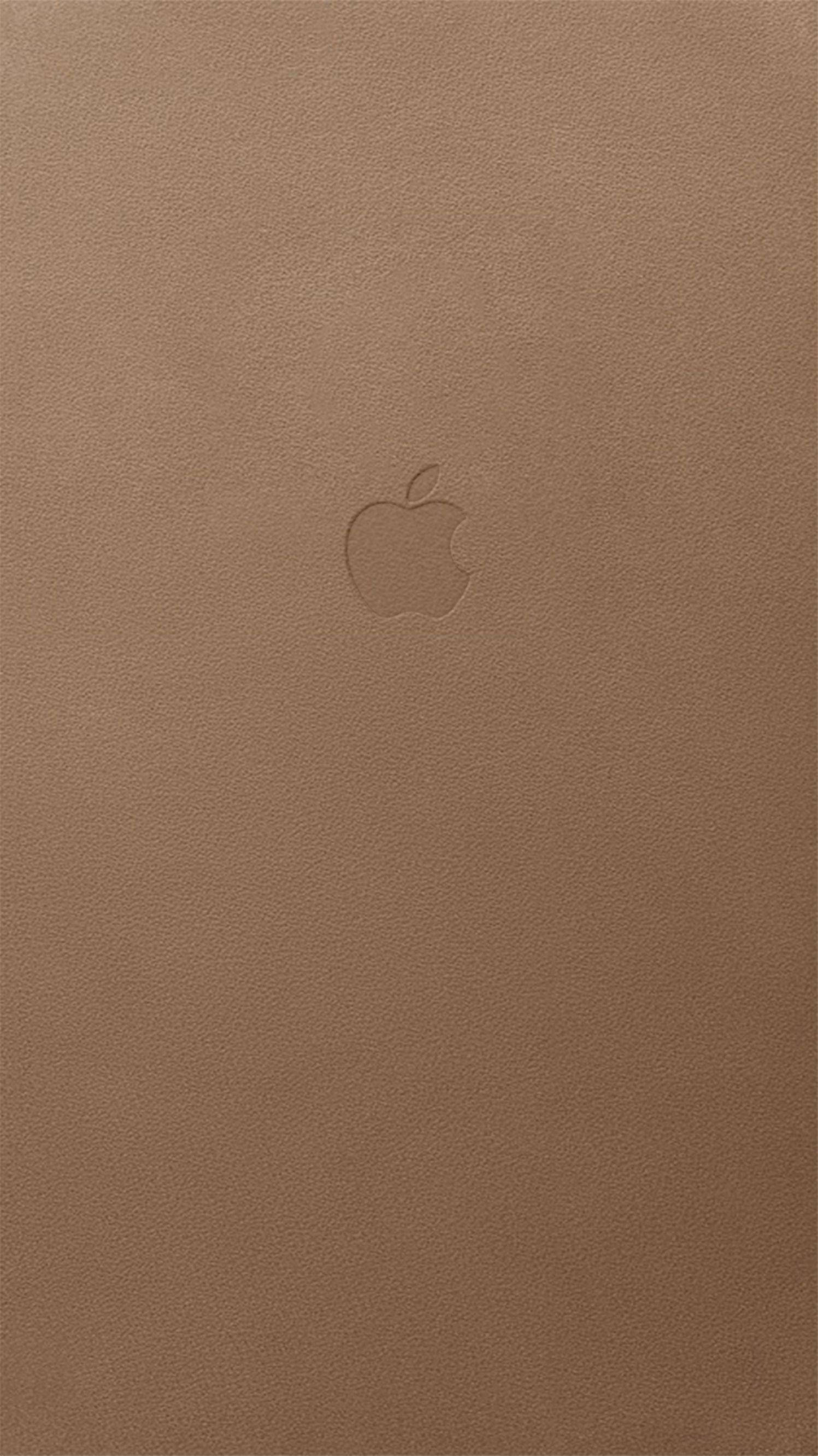 蘋果標誌棕色 iPhone 壁紙 — 一個極簡的淺棕色皮革表面，中央有一個微妙的壓印 Apple 標誌。