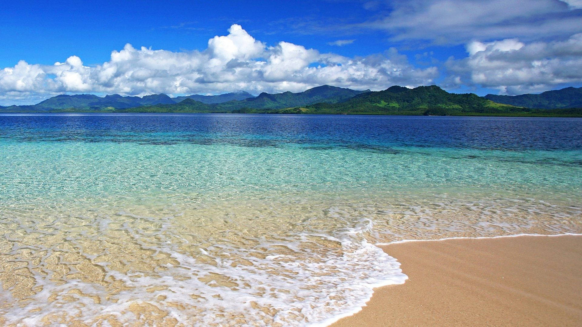 熱帶海灘，碧綠的海水和白色泡沫在藍天白雲下滾上金色沙灘。