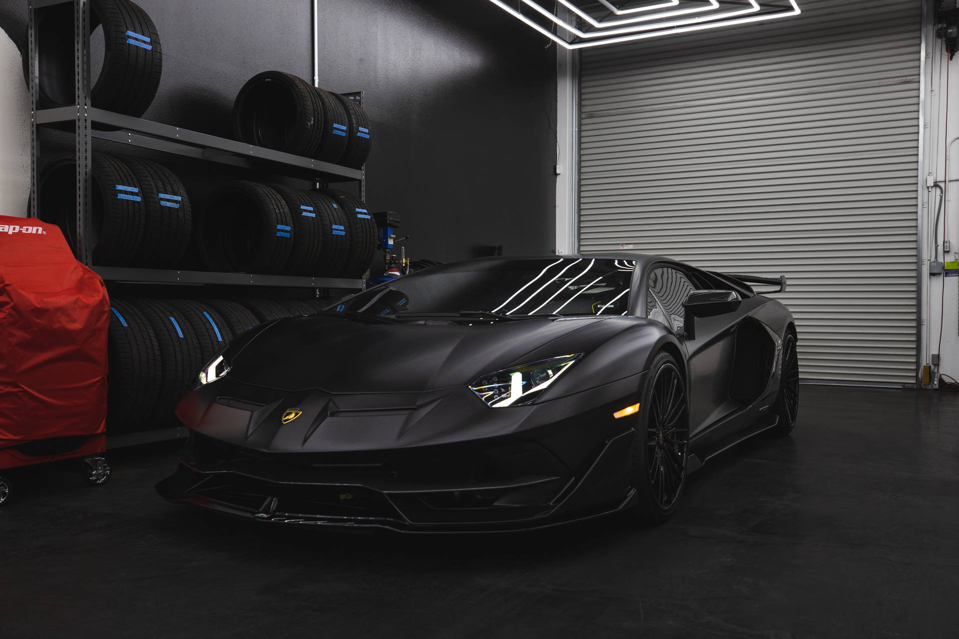 啞光黑色林寶堅尼 Aventador SVJ 在一個高科技車庫中，配有堆疊輪胎。