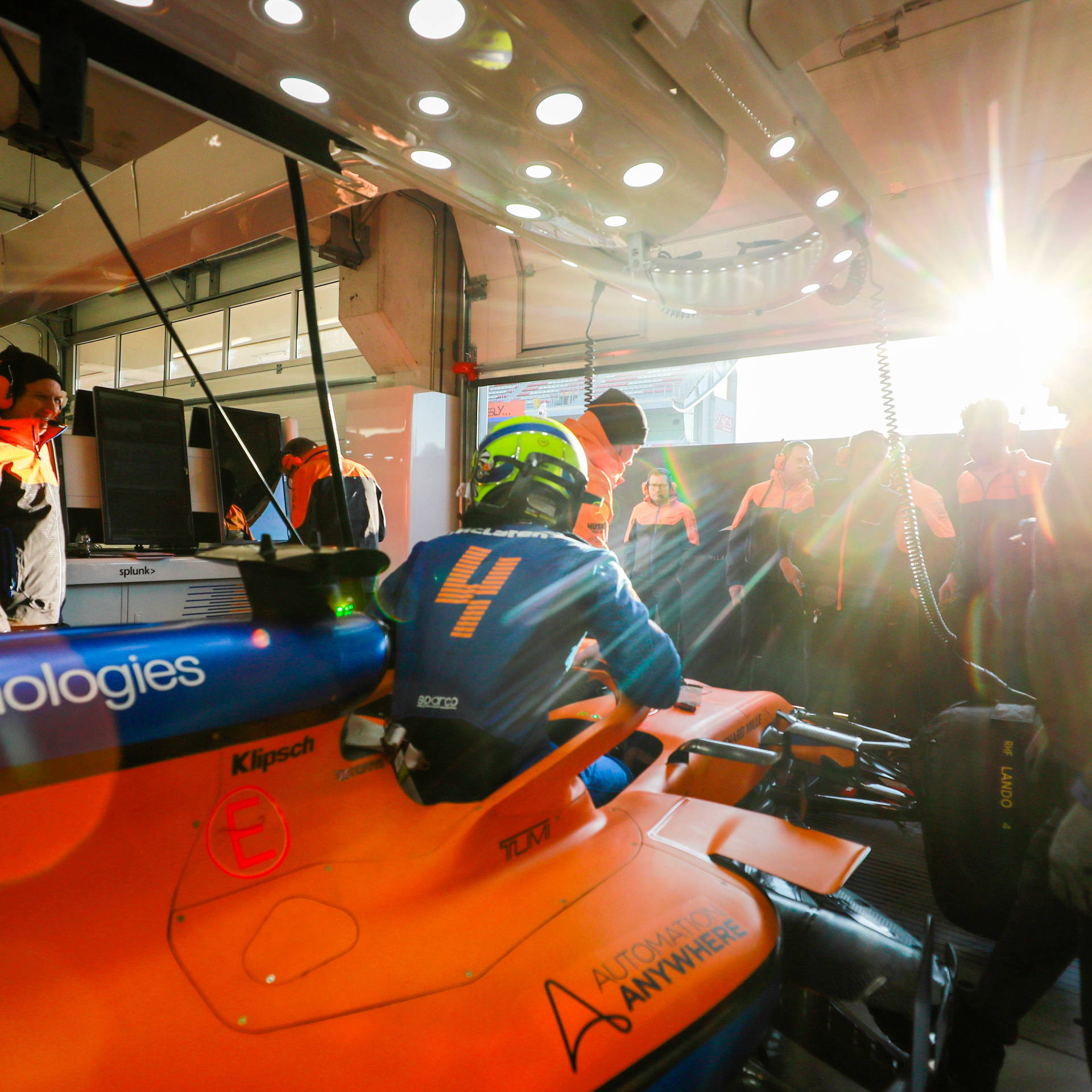 F1車手在橙色賽車中，日落時分在車庫被車隊包圍。