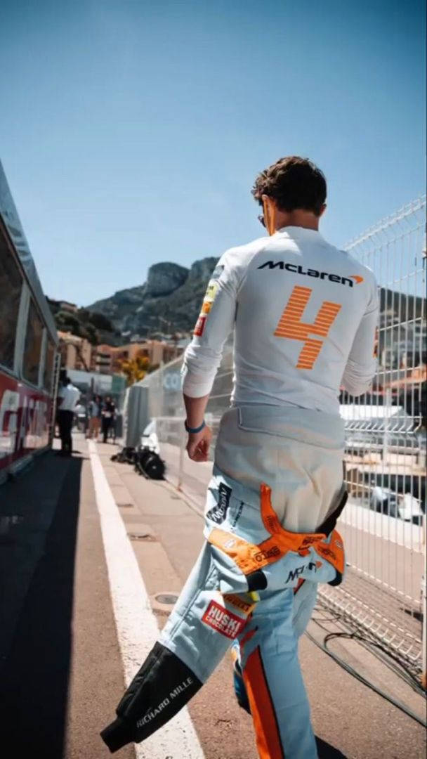 蘭多·諾里斯白色賽車服 壁紙 — 一位賽車手穿著白色McLaren賽車服，號碼4，在陽光明媚的賽道旁小路上遠離鏡頭走去。
