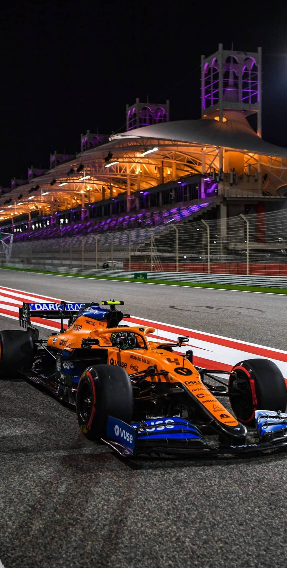 夜間賽道上橙色和藍色的F1賽車，看台燈光璀璨。 — 賽車 壁紙