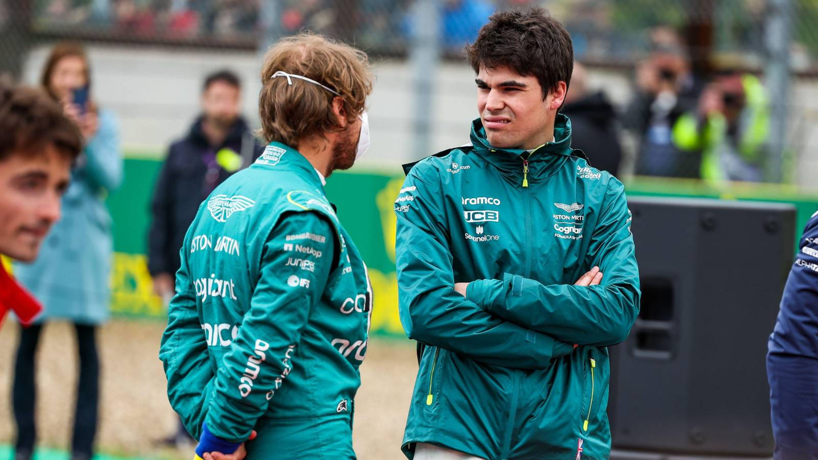 兩名身穿藍綠色車隊外套的F1車手在賽道上交談。