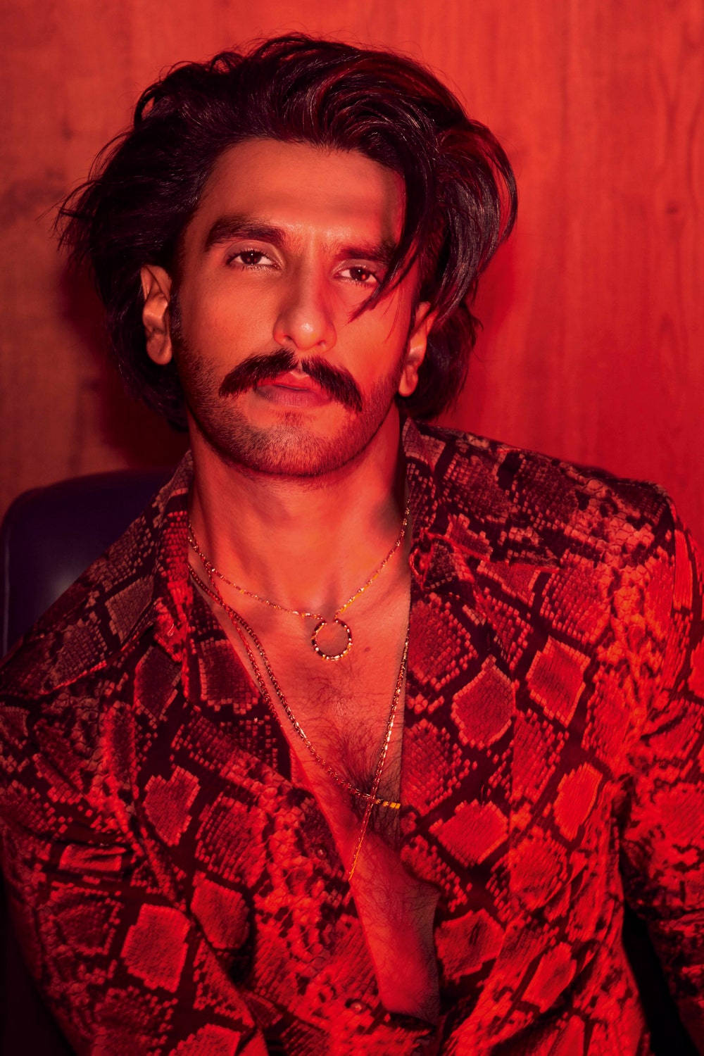 蘭維爾·辛格為《Vogue India》拍攝封面 壁紙 — 一位留鬍子、深色頭髮的男子，在溫暖的紅色燈光下，以木質背景襯托，穿著紅色蛇皮外套。