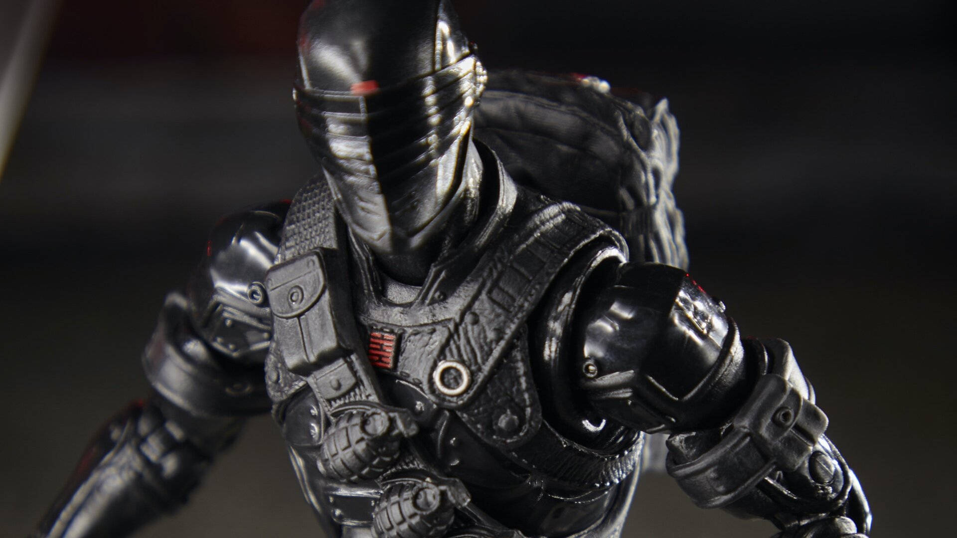 蛇眼的銳利凝視，受尊崇的 G.I. Joe 角色 壁紙 — 黑色裝甲動作人偶的特寫，戴著面具，帶有紅色點綴，背景為深色模糊。