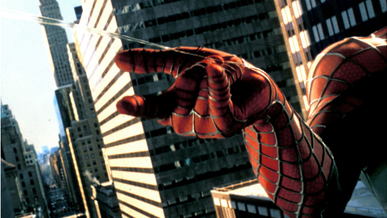 Spider-man Web Shooter 桌布 壁紙 — 蜘蛛俠戴著手套的手向陽光明媚、高樓林立的城市景觀射出蜘蛛網。
