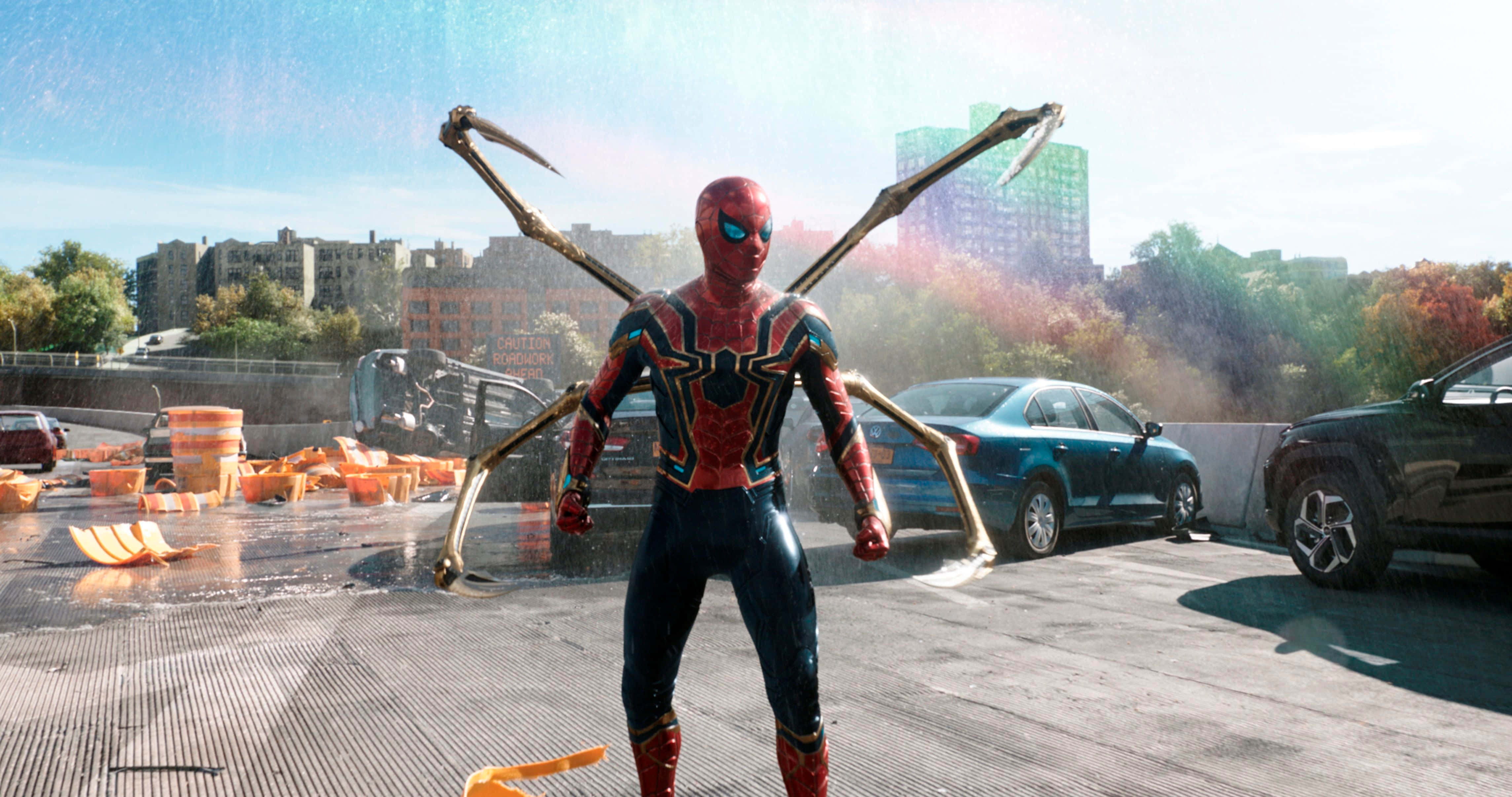Spider Man No Way Home 桌布 壁紙 — 蜘蛛俠身穿紅金色戰衣，站在濕漉漉的屋頂上，四條機械臂在燦爛陽光下伸展開來，映襯著城市天際線。