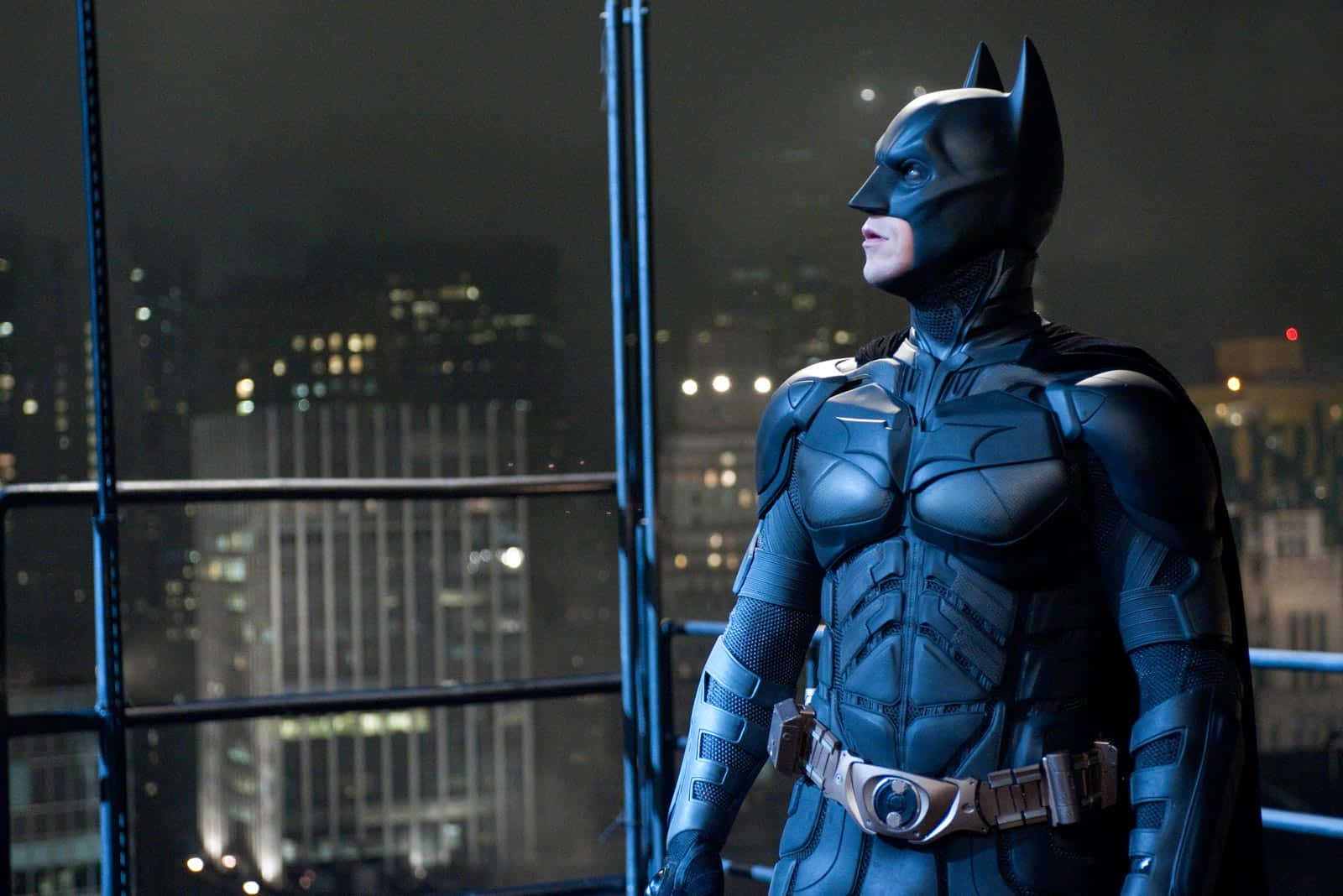 Bat-suit 桌布 壁紙 — 蝙蝠俠在夜晚的黑暗城市景觀中，從高處俯瞰發光的摩天大樓。