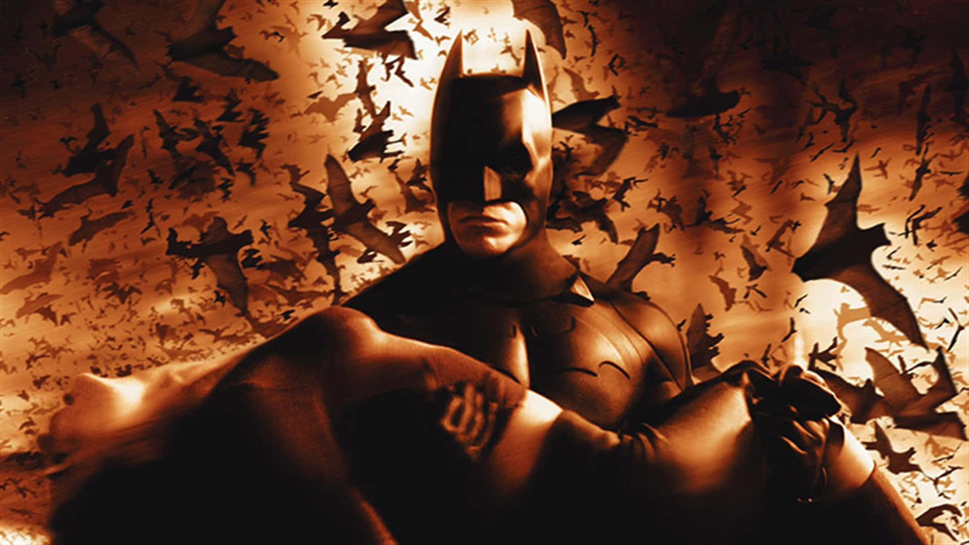 Batman Begins 桌布 壁紙 — 蝙蝠俠堅定地站著，一群蝙蝠在他周圍飛舞，營造出戲劇性的金色場景。