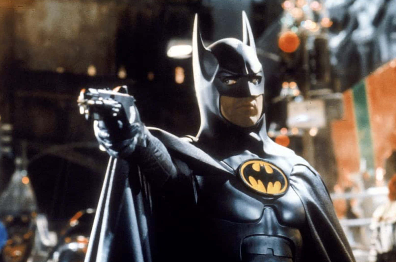 Bat-suit 桌布 壁紙 — 蝙蝠俠穿著他標誌性的黑色西裝，在夜晚的陰暗城市小巷中專注地瞄準一把槍。
