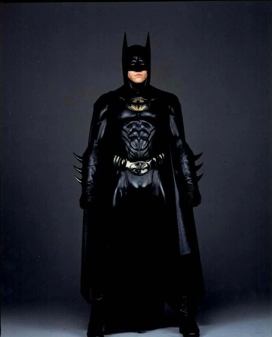 Bat-suit 桌布 壁紙 — 蝙蝠俠穿著全黑裝甲服，披著斗篷和頭罩，站在深色攝影棚背景前。