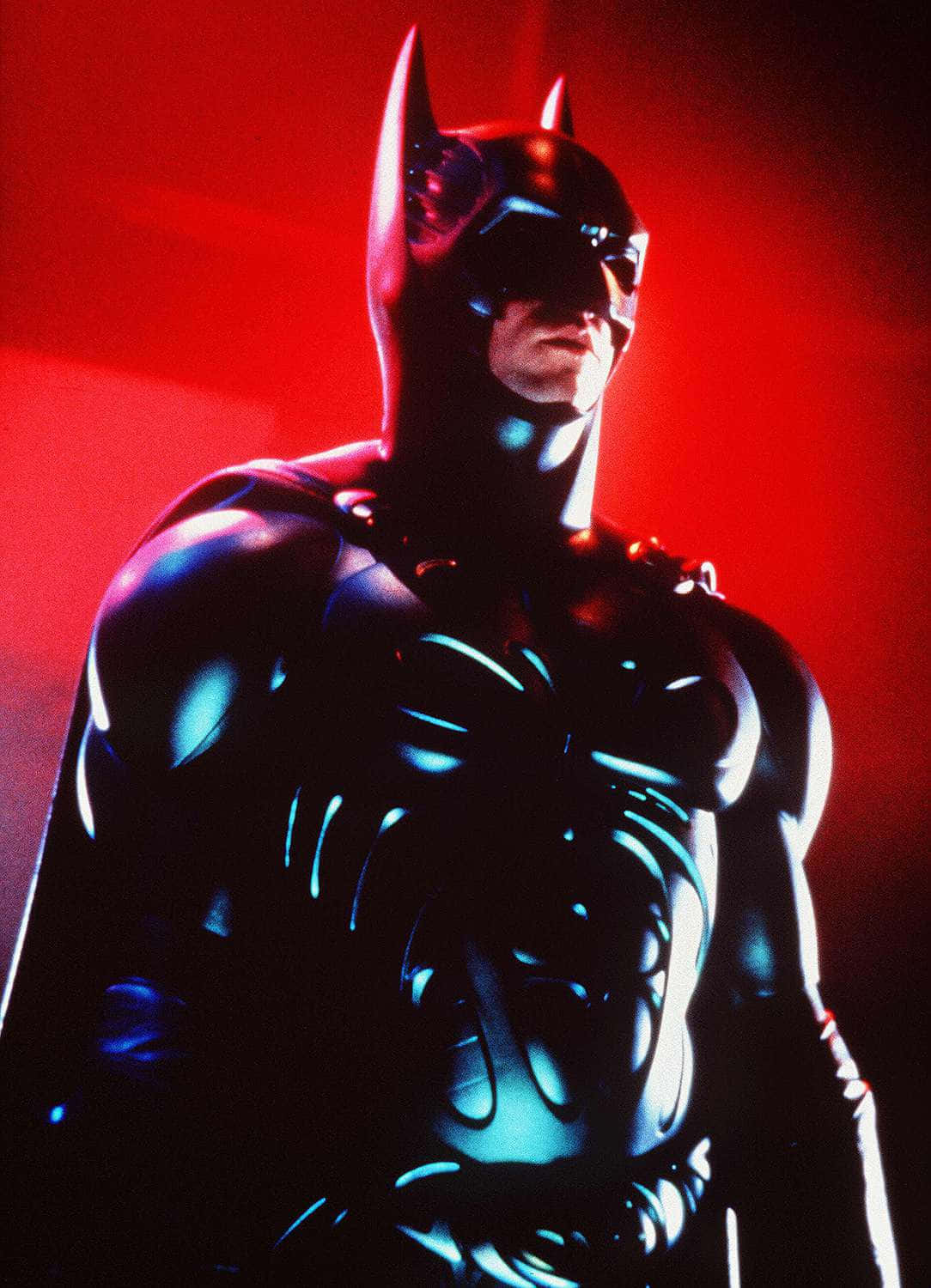 Bat-suit 桌布 壁紙 — 蝙蝠俠站在一個戲劇性的紅光場景中，他的裝甲服上帶有發光的藍色亮點。