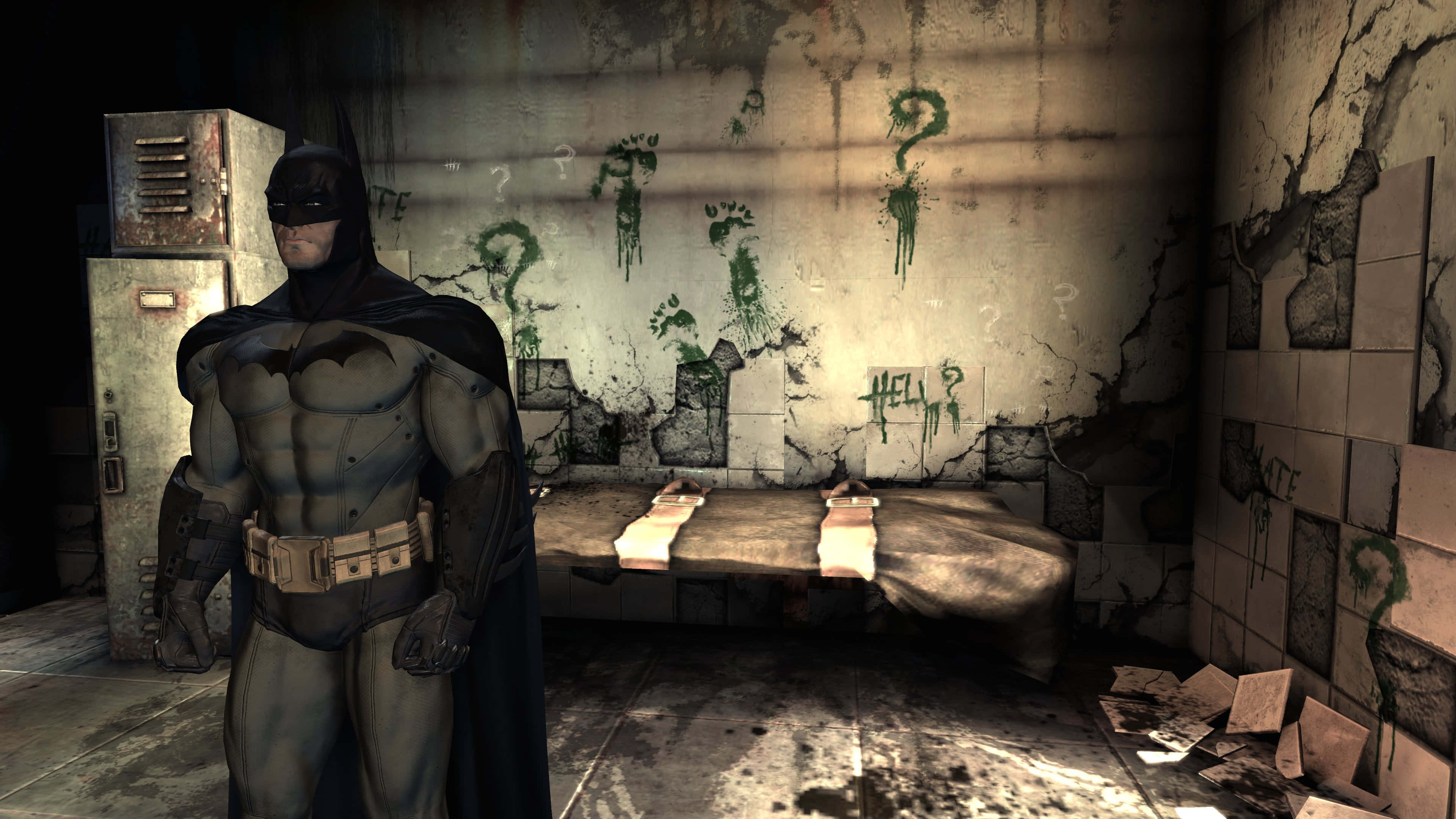 Arkham Asylum 桌布 壁紙 — 蝙蝠俠站在一個骯髒、佈滿塗鴉的牢房裡，有生鏽的儲物櫃和破損的瓷磚，光線昏暗。