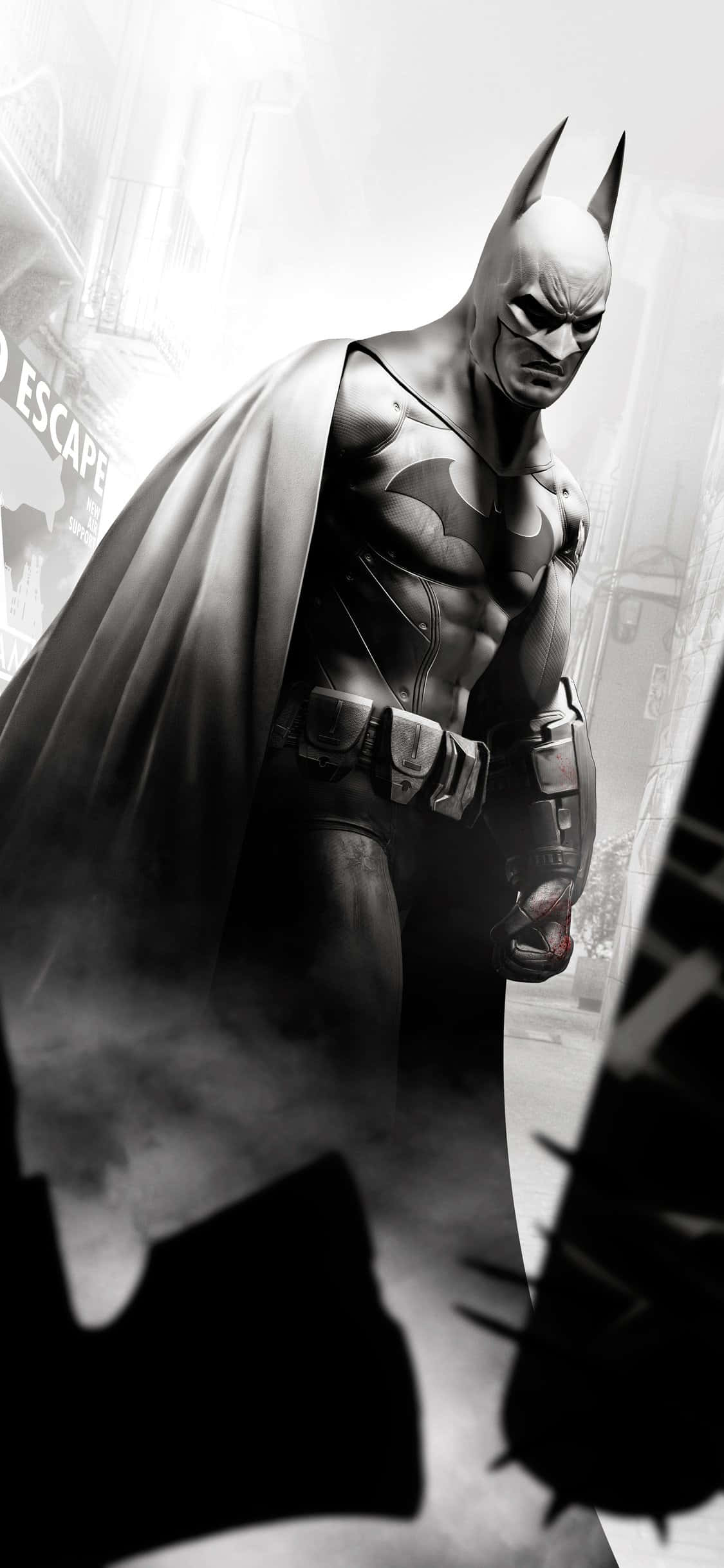 Batman Arkham Knight 桌布 壁紙 — 蝙蝠俠站在粗糙的黑白城市景觀中，斗篷飄揚，面具嚴肅，周圍環繞著煙霧般的陰影和模糊的城市衰敗。