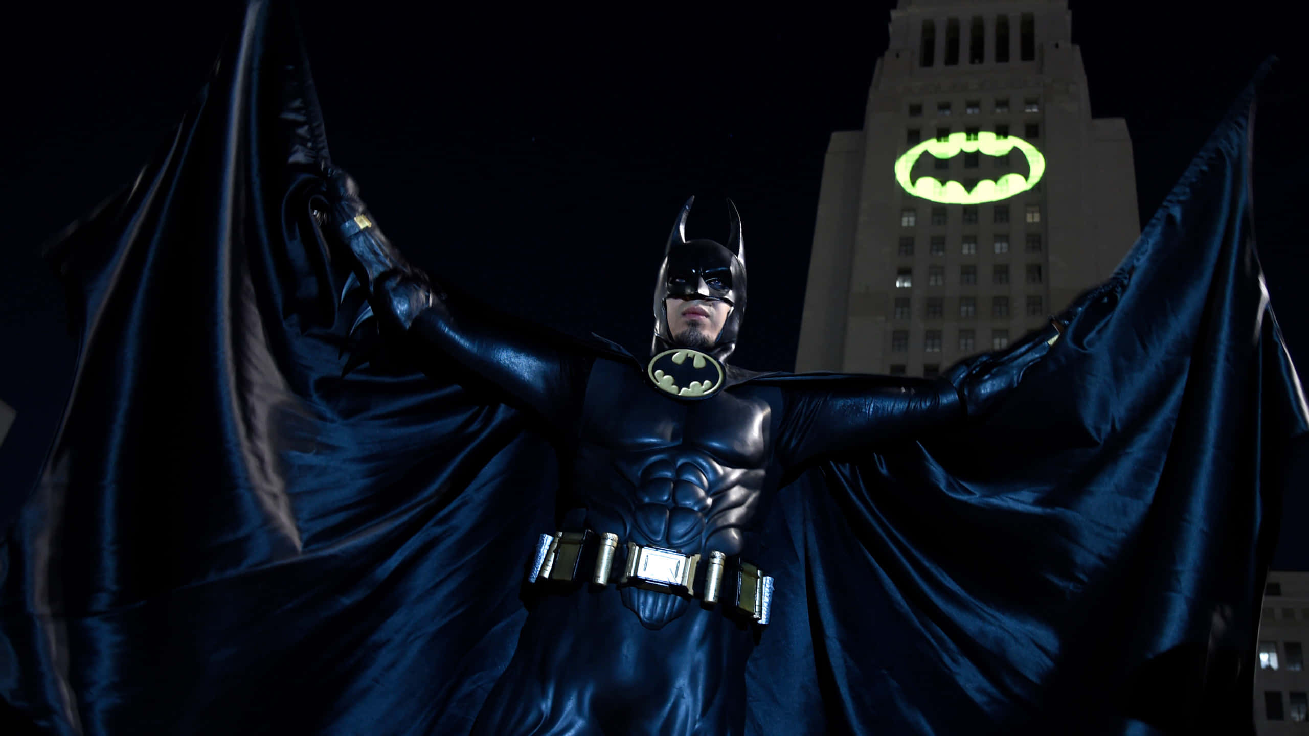 Bat Signal 桌布 壁紙 — 蝙蝠俠英雄地站在黑暗的城市天際線前，斗篷張開，建築物上有一個發光的蝙蝠標誌。