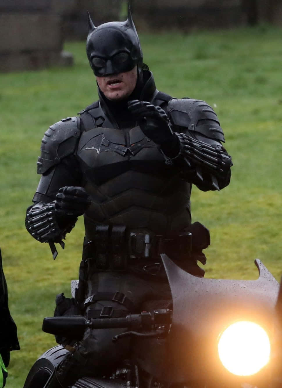 Bat-suit 桌布 壁紙 — 蝙蝠俠身穿全副盔甲，騎著一輛帶有發光頭燈的電單車穿過草地。