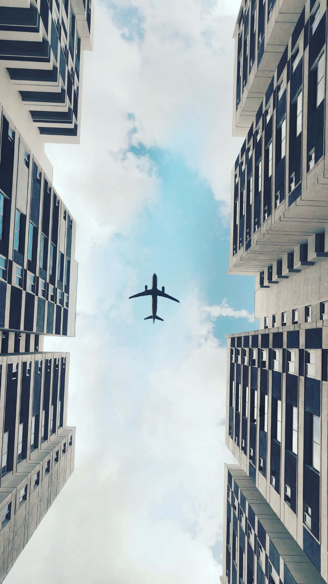 飛機在藍天白雲下飛越城市高樓之間。