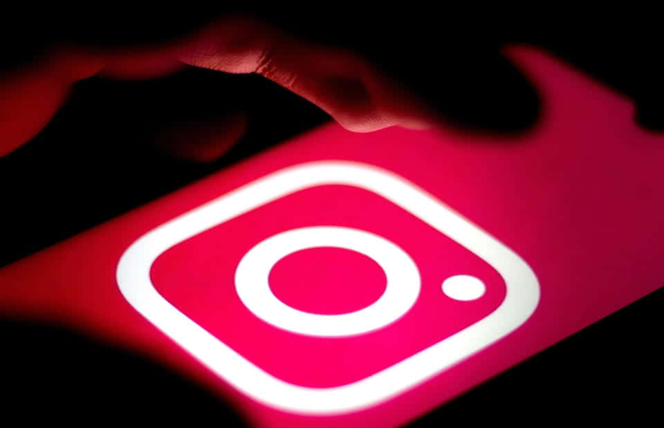 手在夜間懸浮在發光的Instagram應用程式圖標上方。
