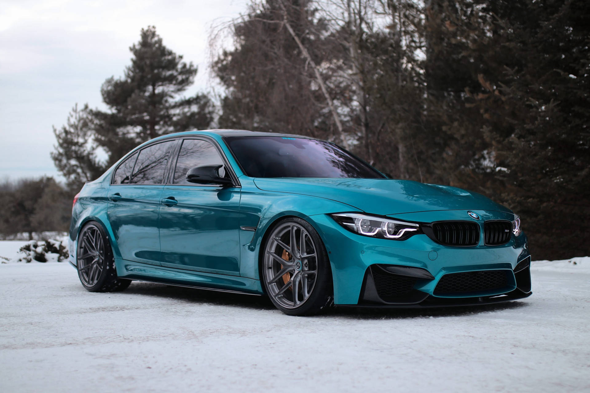 綠松石色BMW M3房車停泊喺樹附近嘅雪地上。