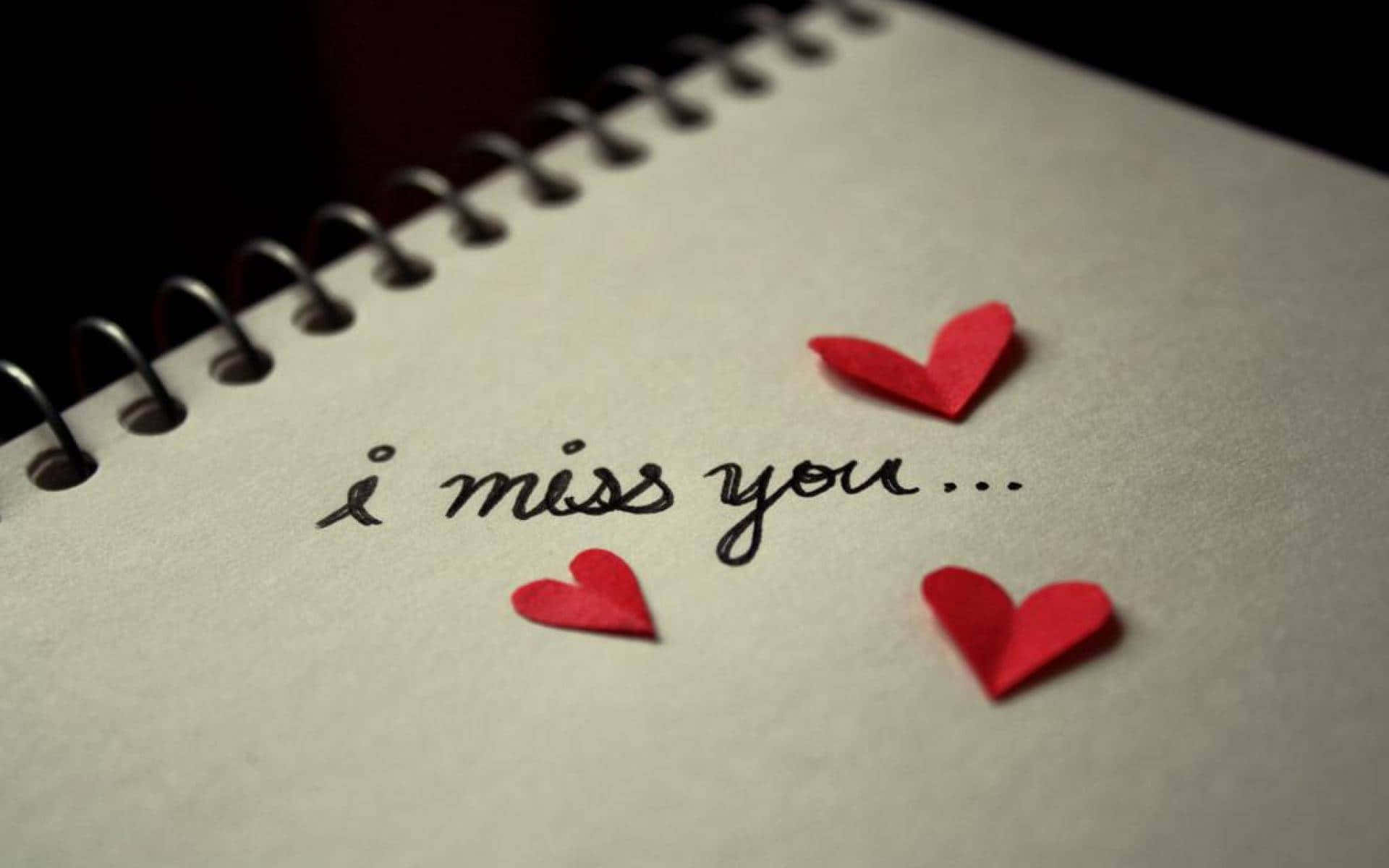 I Miss You 桌布 壁紙 — 螺旋裝訂筆記本的近距離特寫，上面有手寫文字「我想你」，附近散落著三個紅色紙心。