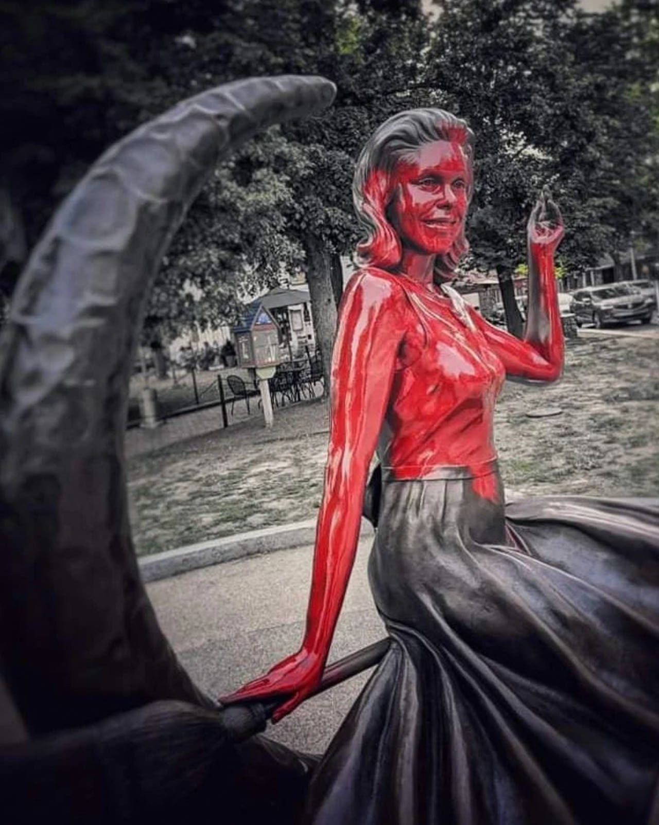 一座漆成紅色的女性雕像，穿著黑色裙子，在公園中透過彎曲的拱門觀看。