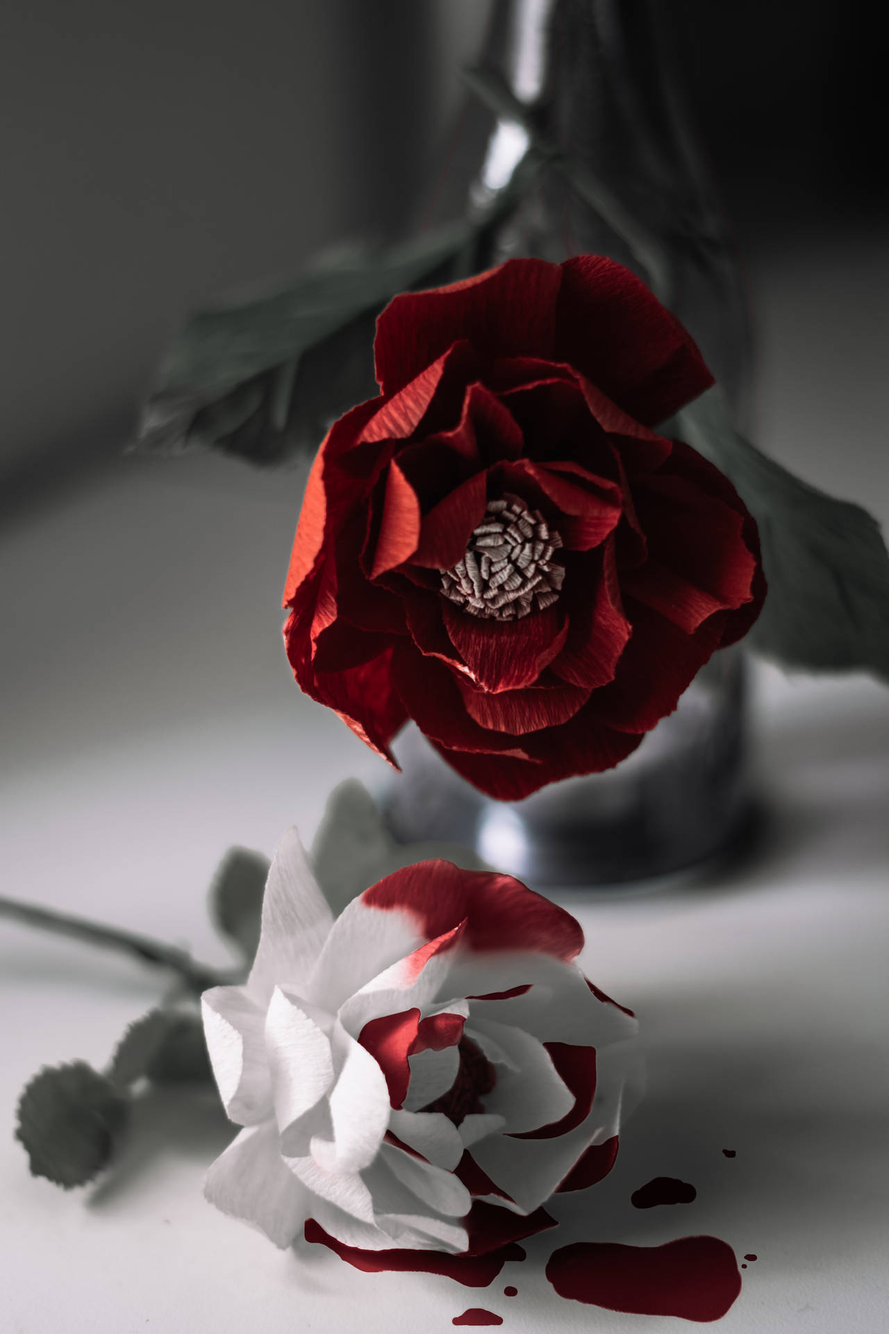 花瓶中的紅色紙玫瑰與一朵在白色表面上滲出紅色液體的白色紙玫瑰。